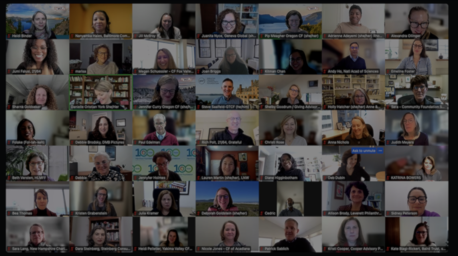 A large group of people smiling and posing in individual boxes during a virtual video call, each person appearing in their own home or office background.
