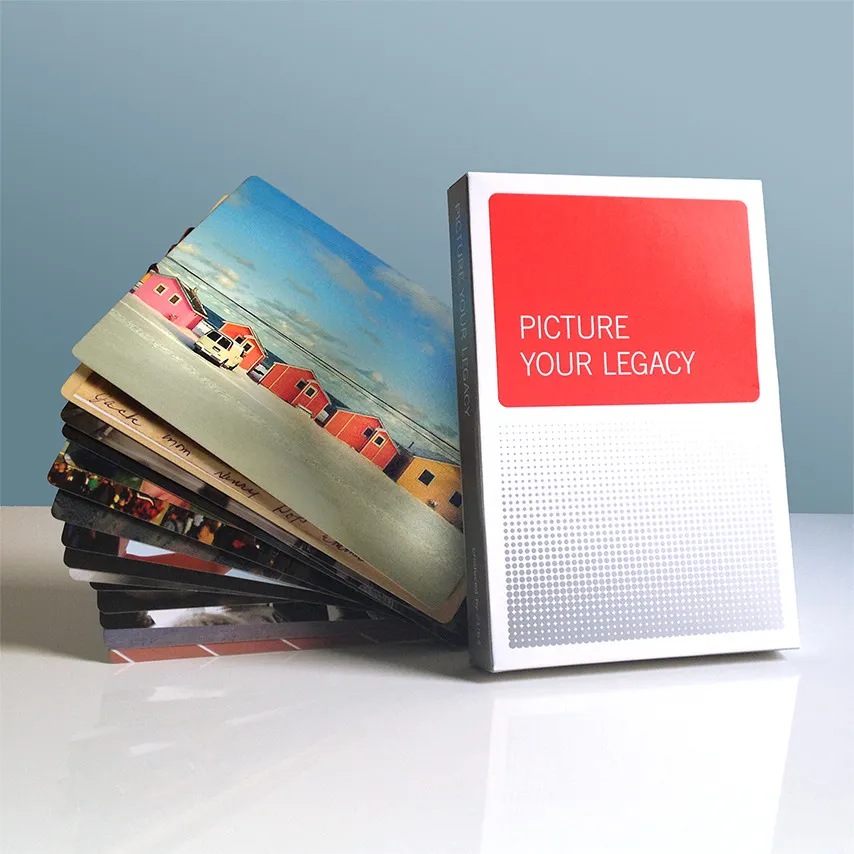 A stack of colorful picture cards leans against a box labeled Picture Your Legacy with a red and white design, all set on a reflective surface with a light blue background.
